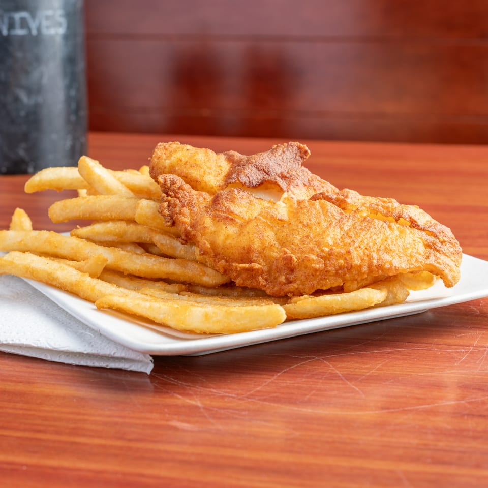 Crispy golden-brown fish and chips on a white plate with a dark background.