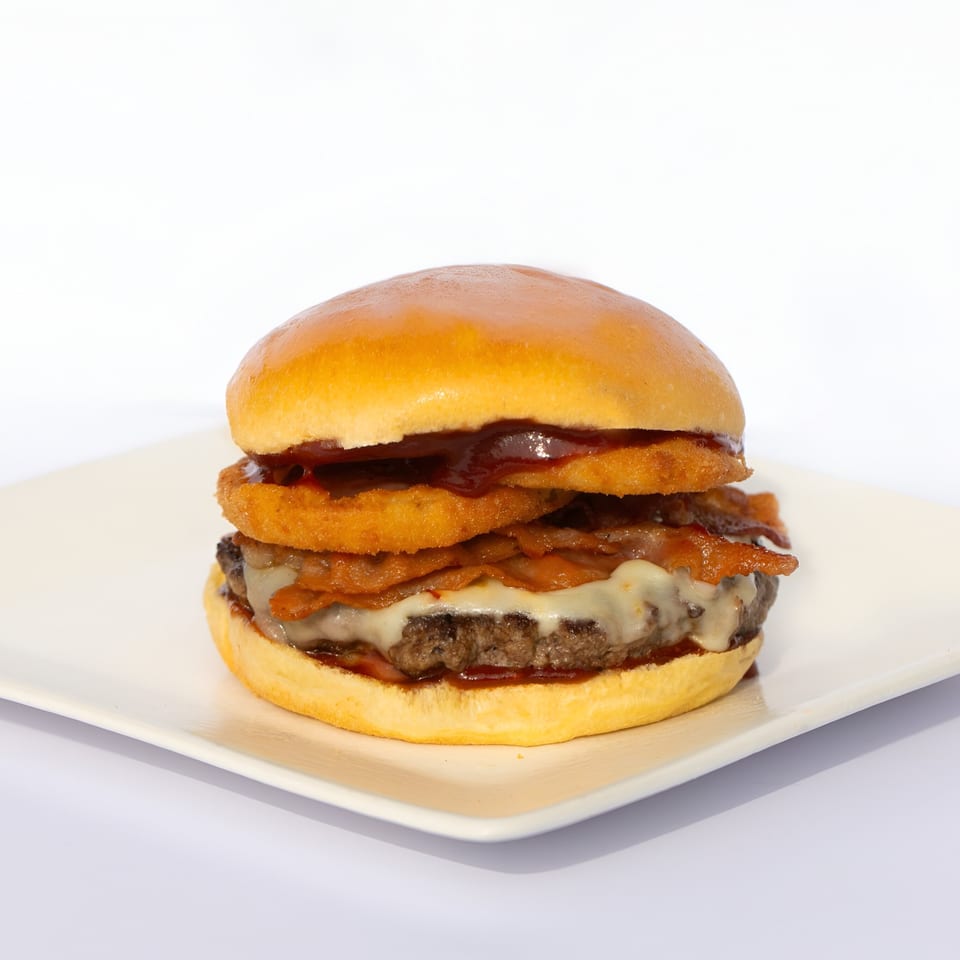 Morehead Burger with melted cheese, crispy bacon, onion rings, and barbecue sauce on a white plate.