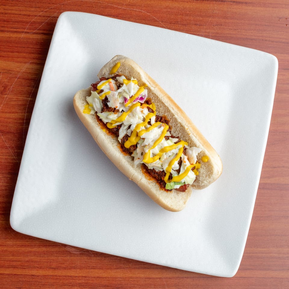 A Morehead Burger Company hot dog with chili, coleslaw, and mustard on a white plate.