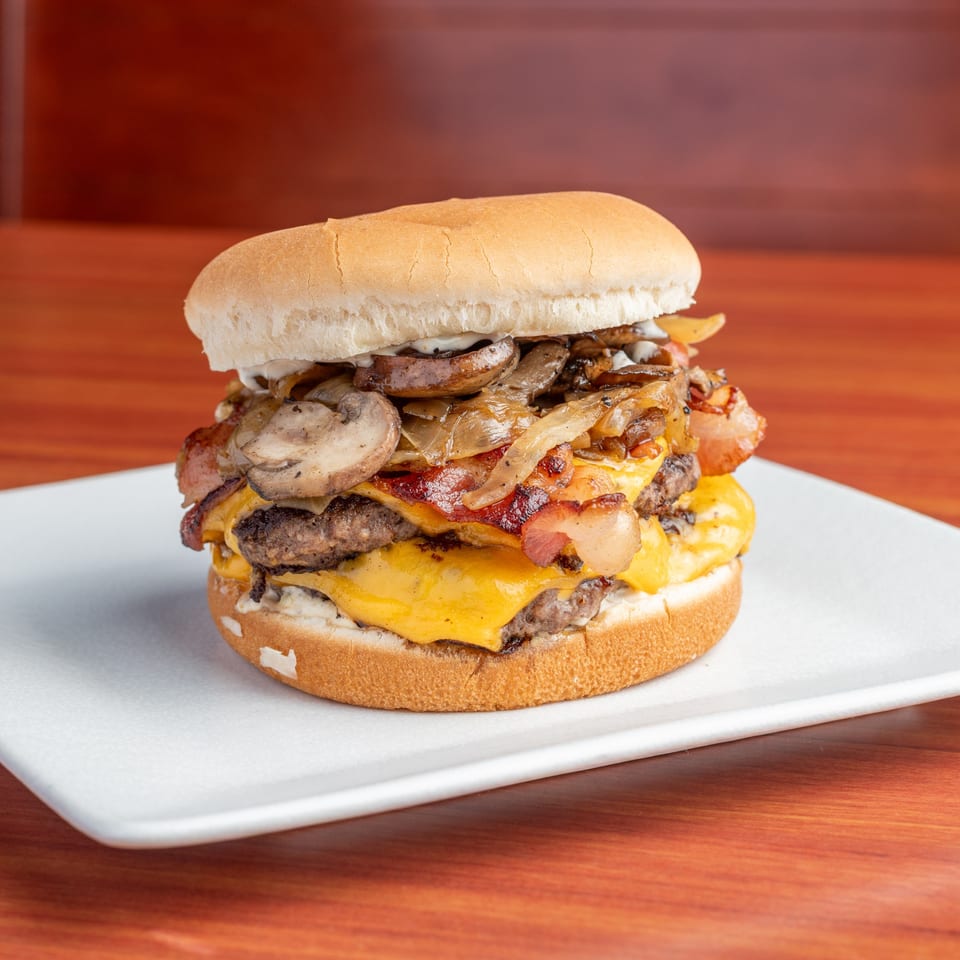 Morehead Burger Company's double cheeseburger with bacon, grilled onions, and mushrooms on a white plate.