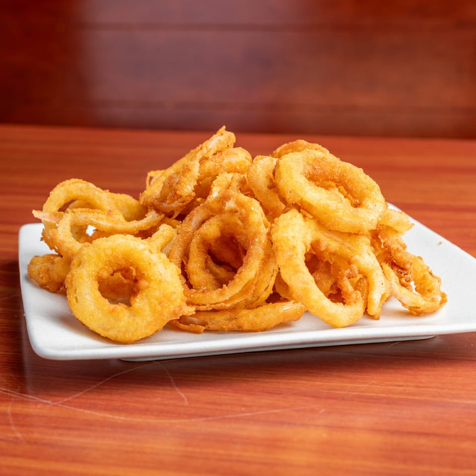 A white rectangular plate piled high with golden-brown, crispy onion rings on a wooden table.