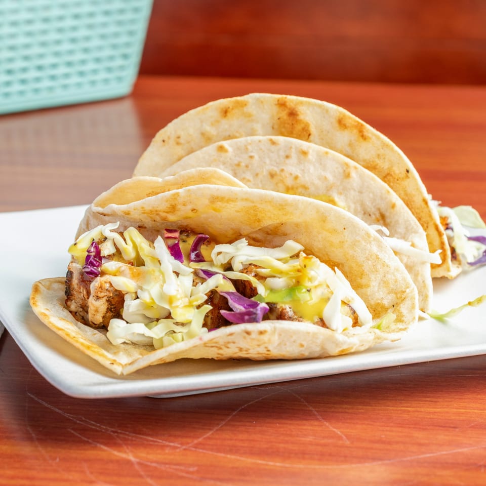 Three chicken tacos with shredded cabbage and purple cabbage on a white plate.