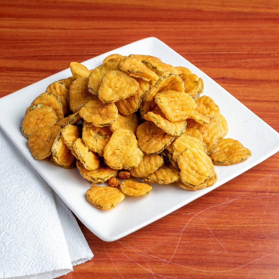 A white rectangular plate piled high with golden-brown fried pickles, on a wooden table.